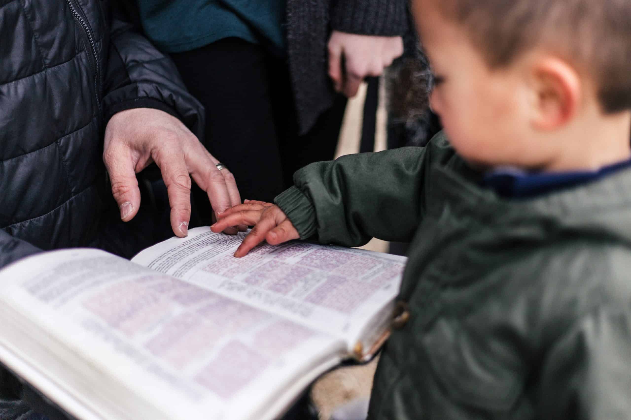 an adult holding an open bible and a child pointing to the text